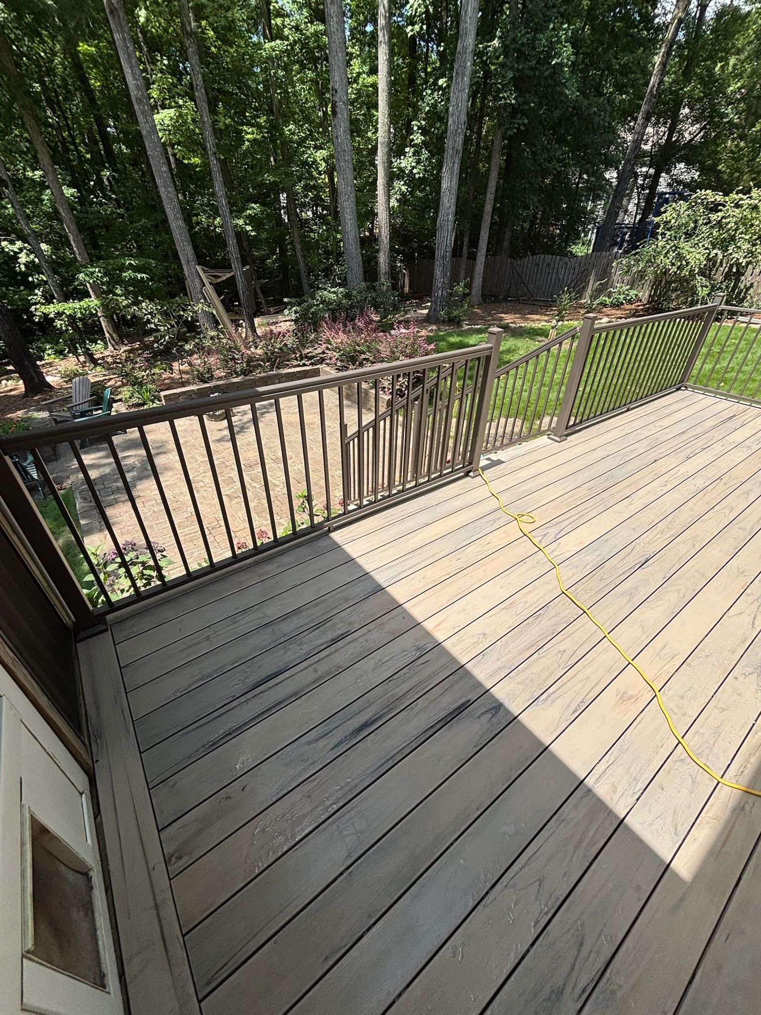 Wooden deck with black railing overlooking a wooded yard in bright sunlight