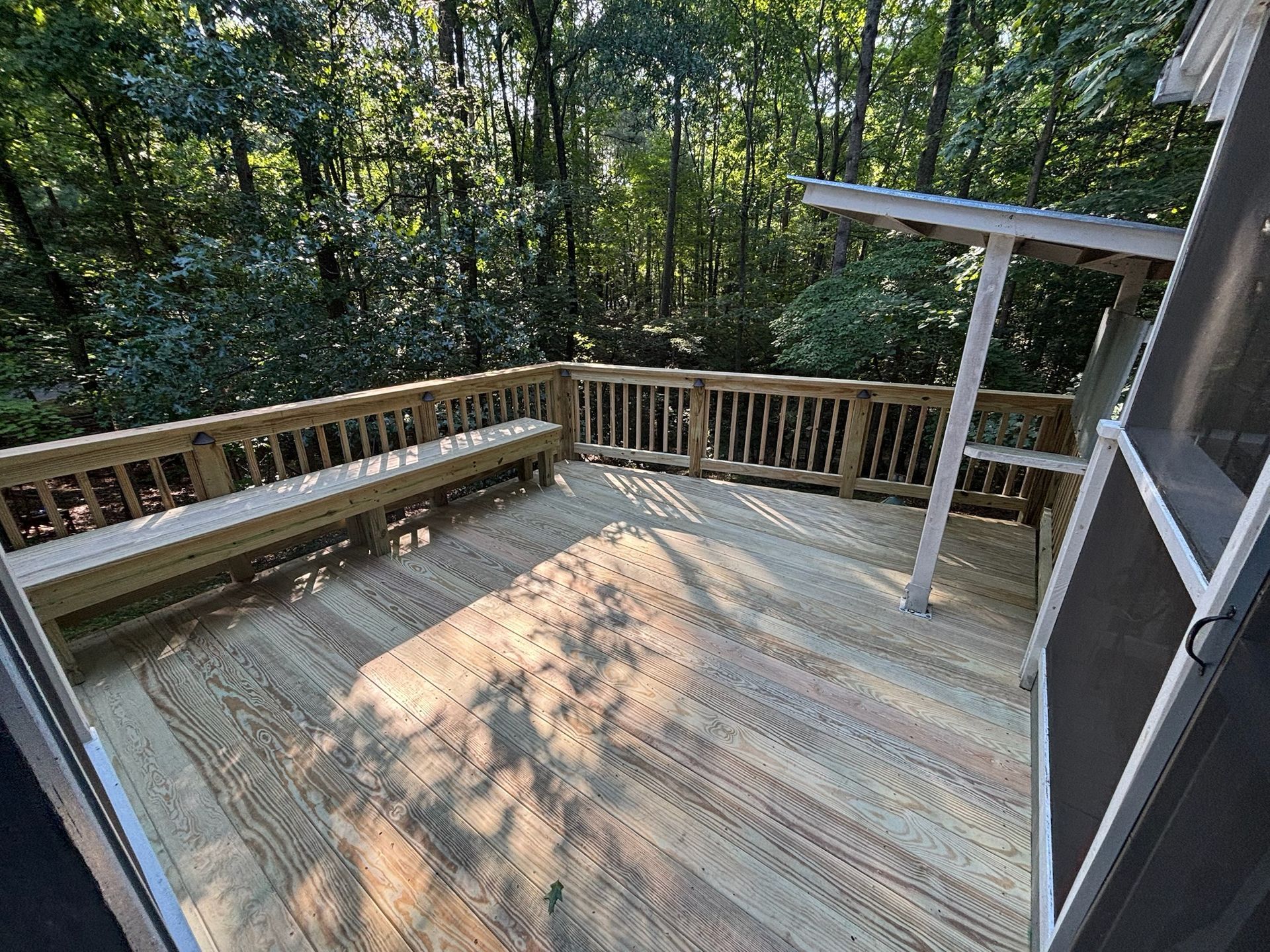Wooden deck with built-in bench overlooking a wooded area, lit by sunlight.