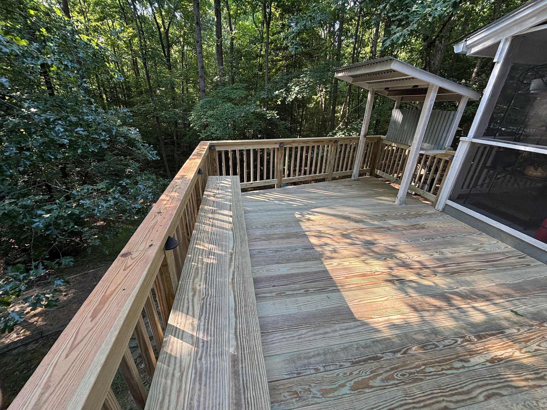 Wooden deck with railing and pergola beside a wooded backyard.