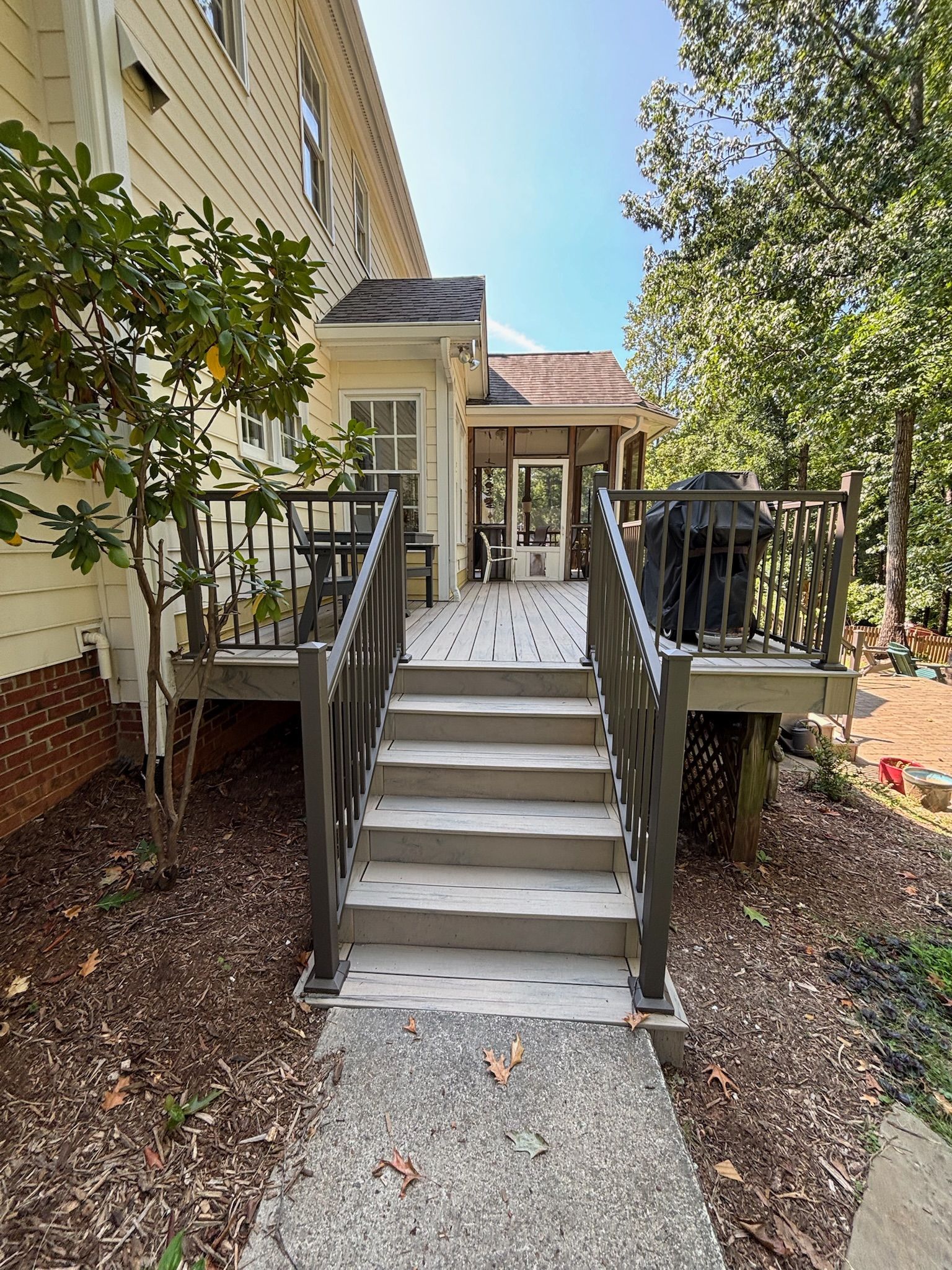 Front stairs with gray handrails leading to a house entrance, flanked by small porches and shrubs.