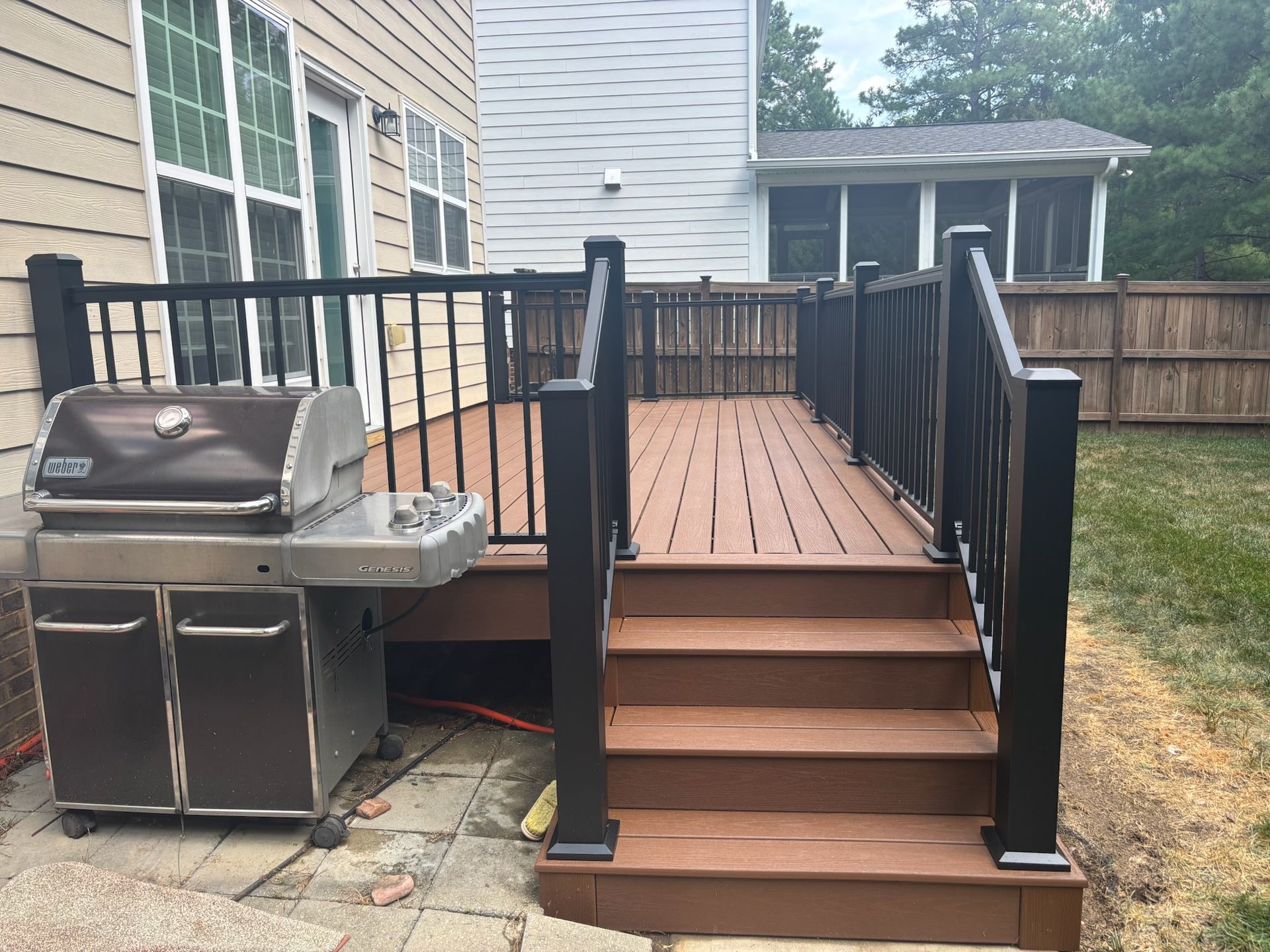 Backyard wooden deck with stairs, black railings, and a stainless steel grill beside a house