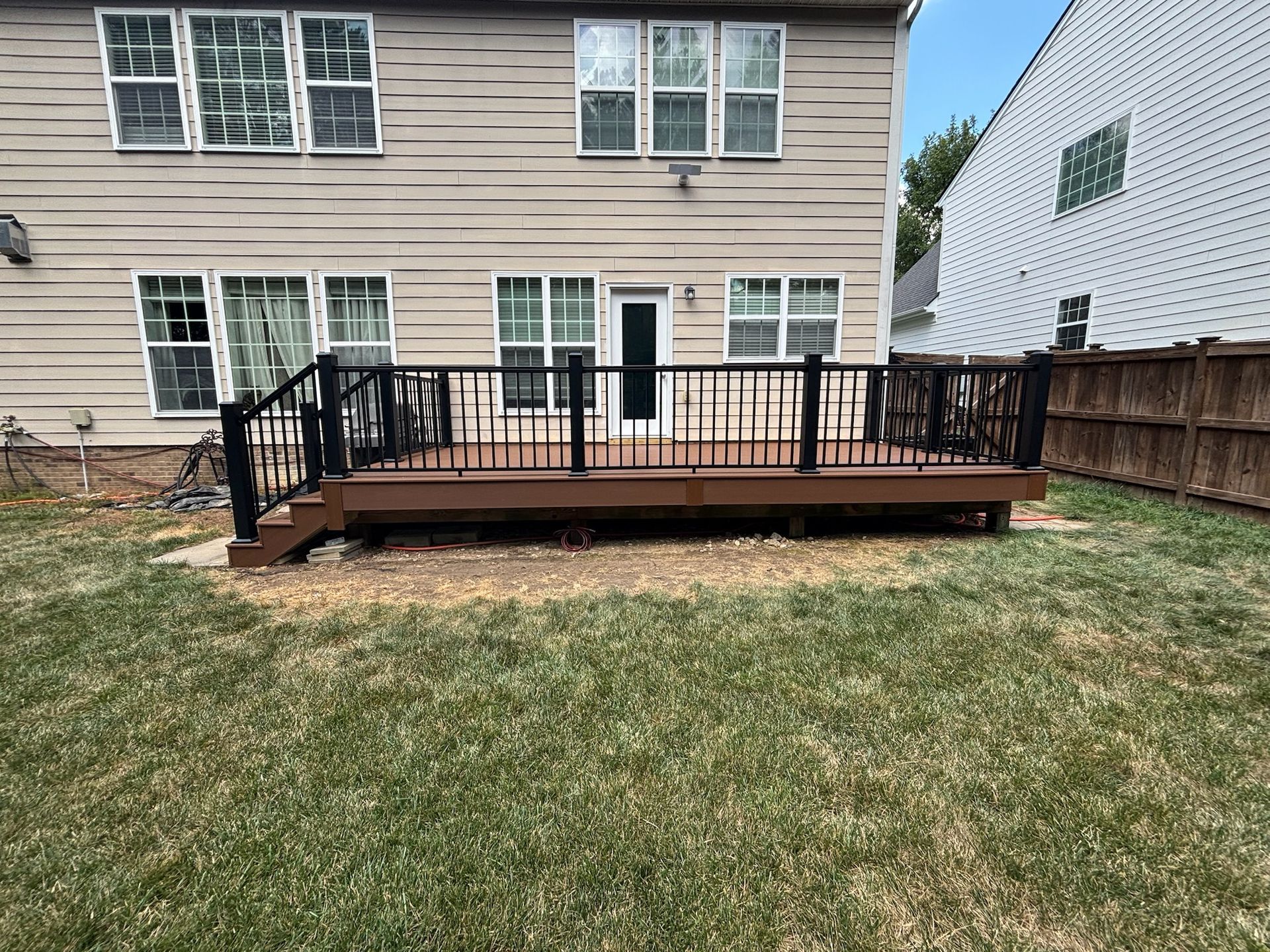 Back deck with black railing attached to a beige house, overlooking a grassy backyard