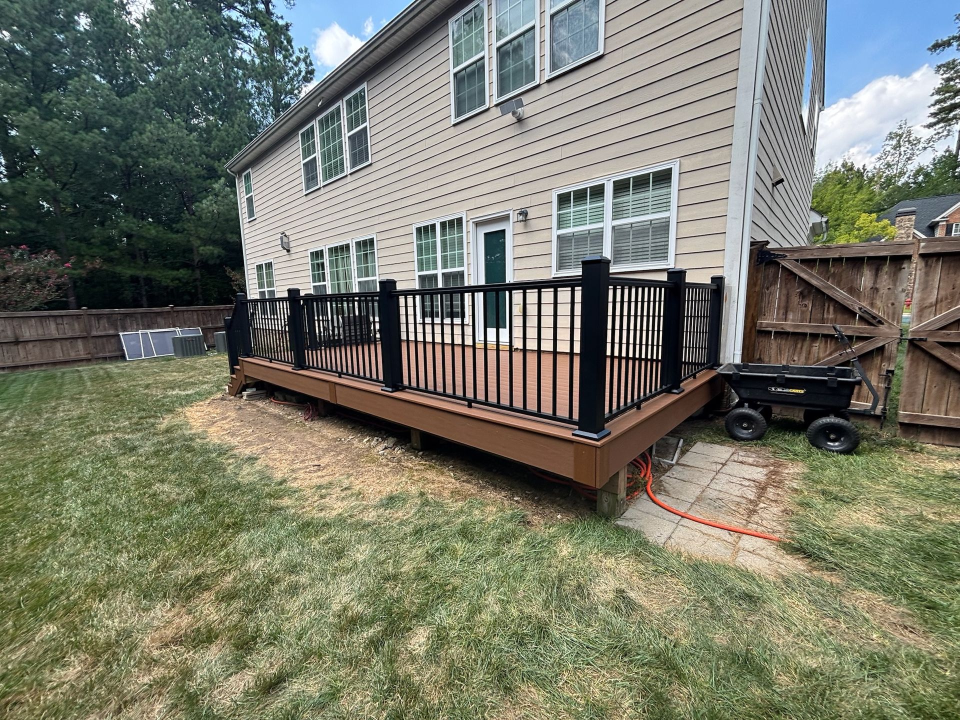 Backyard wooden deck with black railings beside a beige house and fenced yard