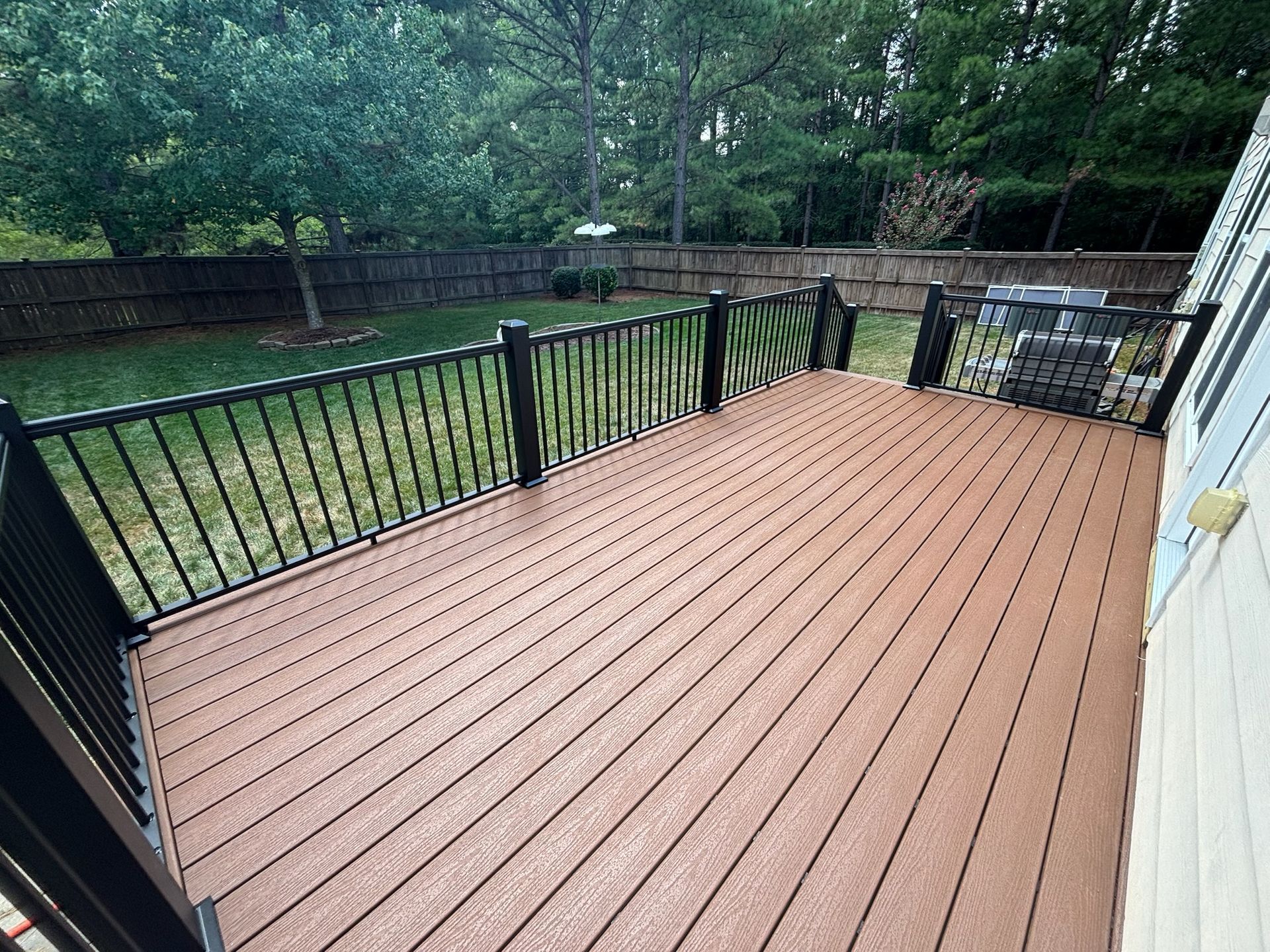 Backyard deck with brown composite flooring, black railing, and grassy yard with trees beyond