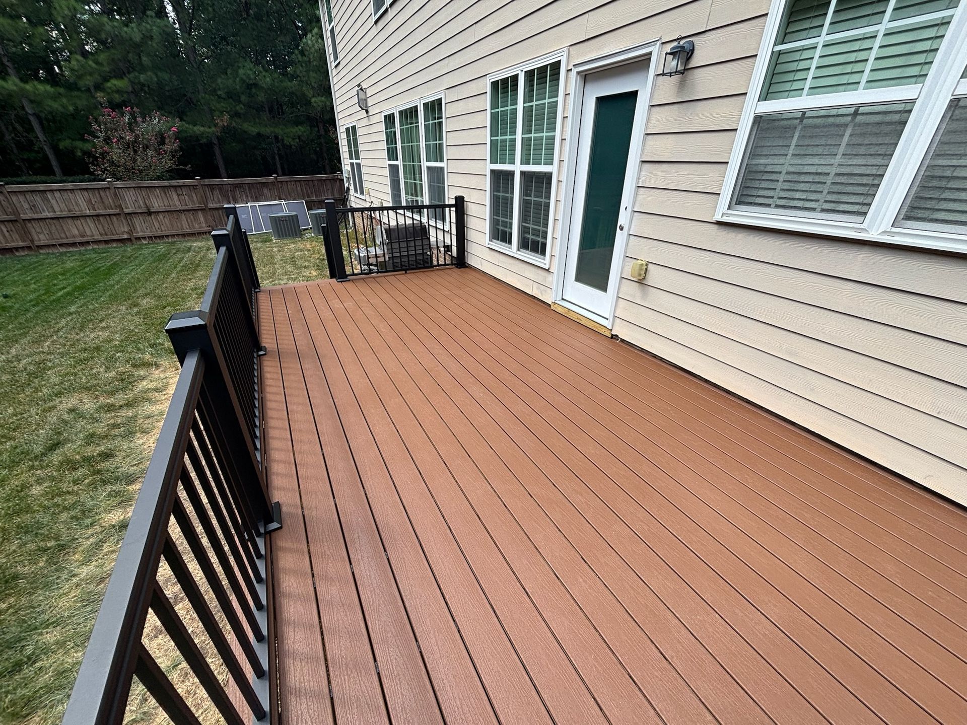 Wooden deck with black railing beside beige house and sliding glass door, overlooking a grassy yard