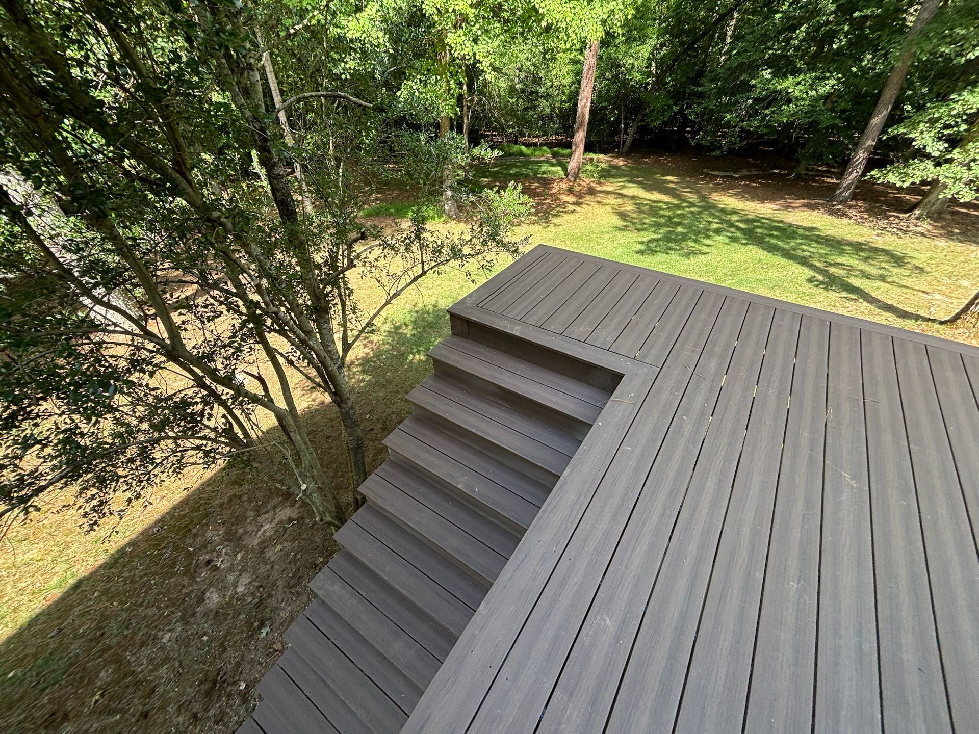 Gray rooftop deck overlooking a wooded backyard with trees and grass