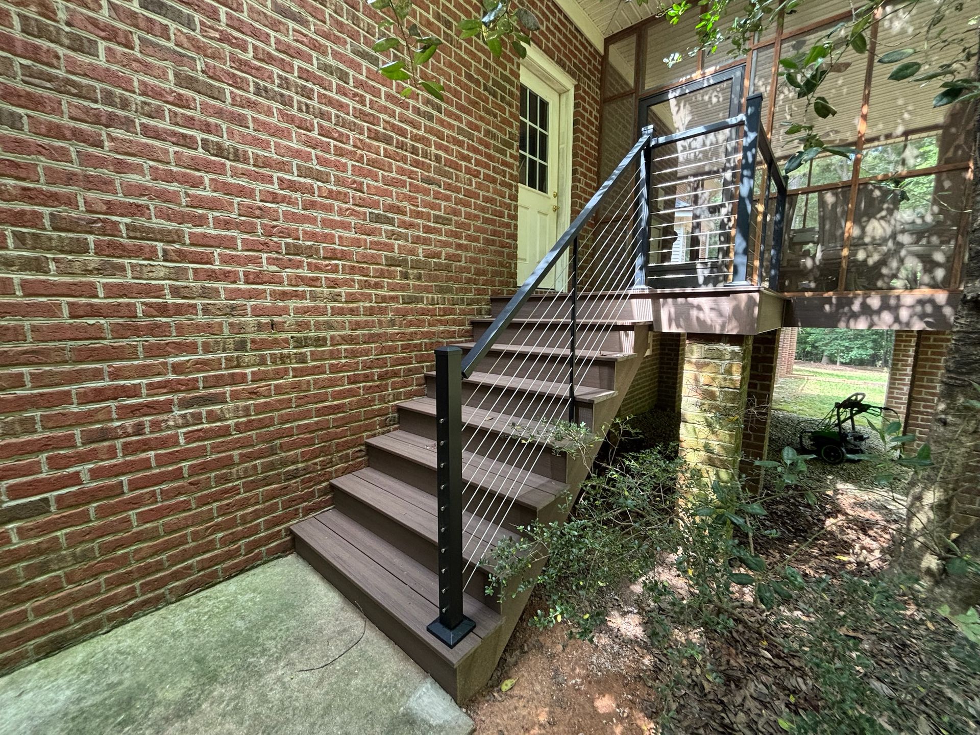 Outdoor metal stairway beside a brick wall, leading to a raised walkway with black railings.