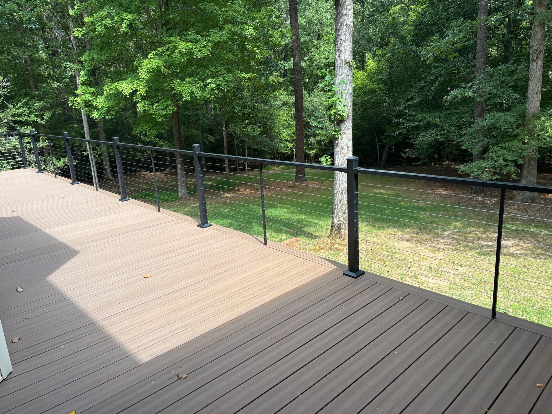 Wooden deck overlooking a grassy yard and trees, with black railing along the edge.