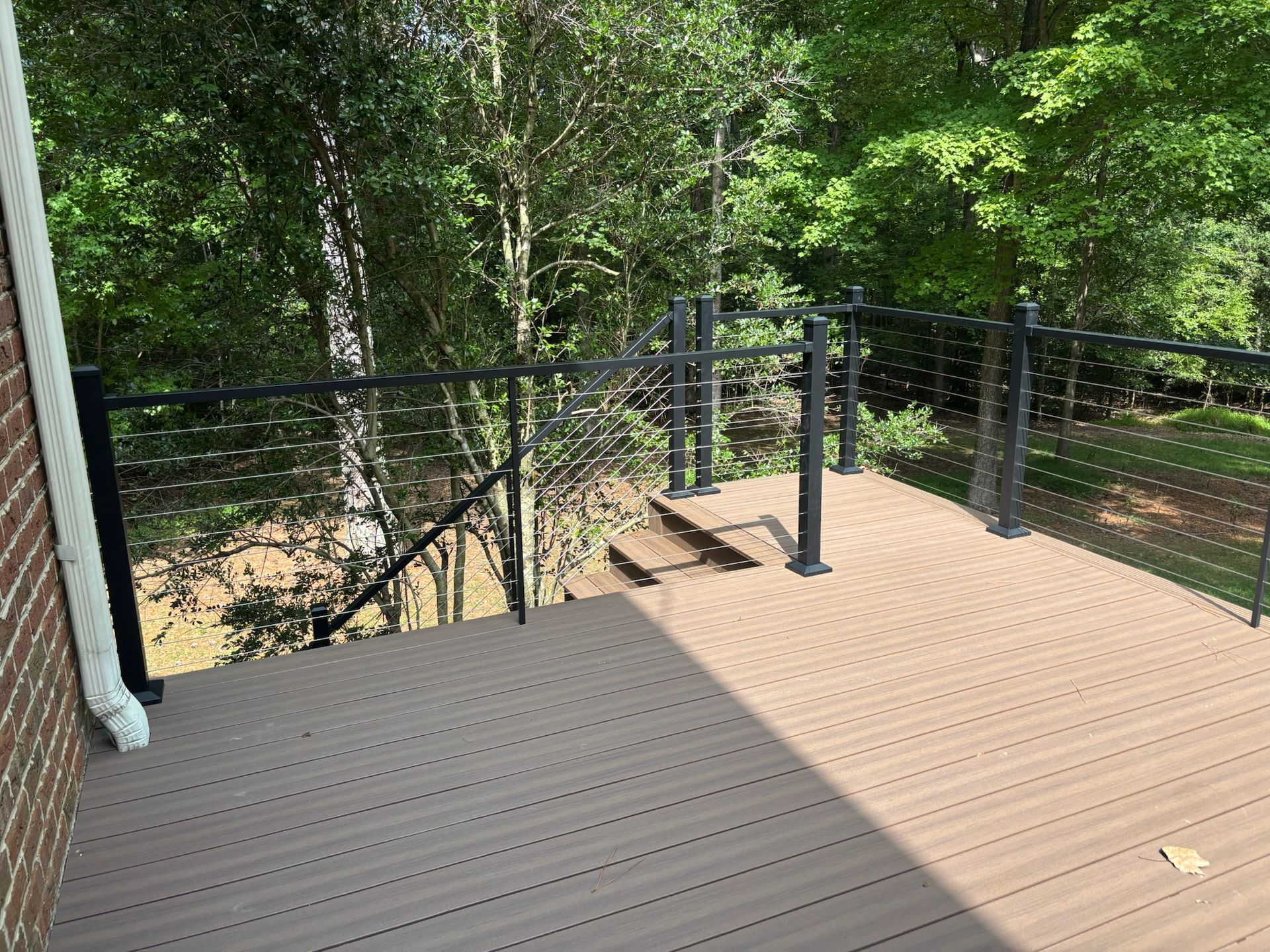Wooden deck with black railing overlooking a wooded backyard and a dirt path below
