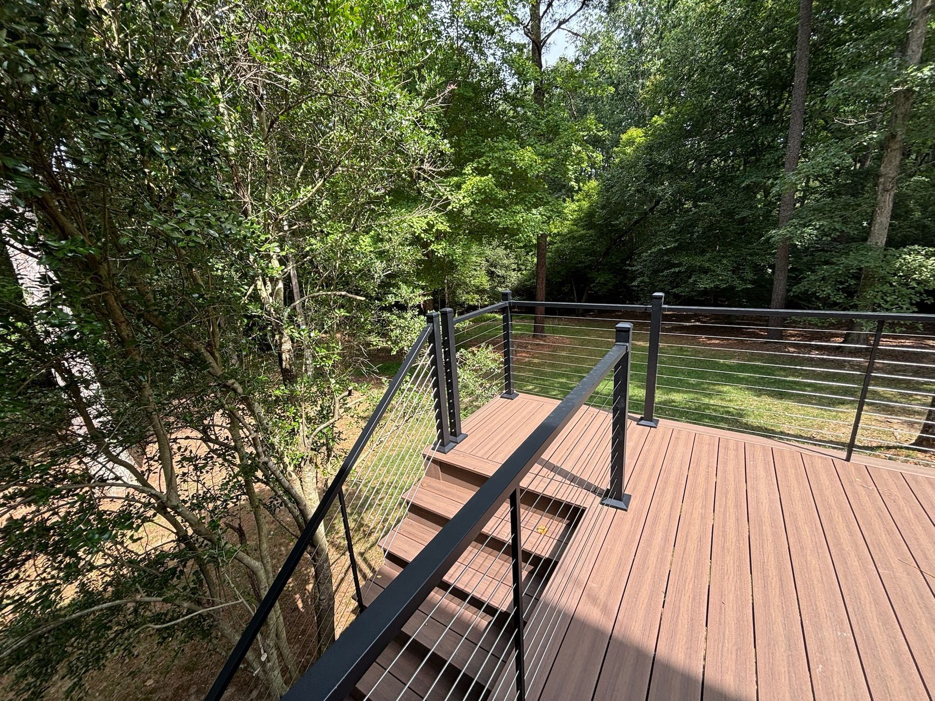 Wooden boardwalk deck with black railings, overlooking dense green woods and a creek below