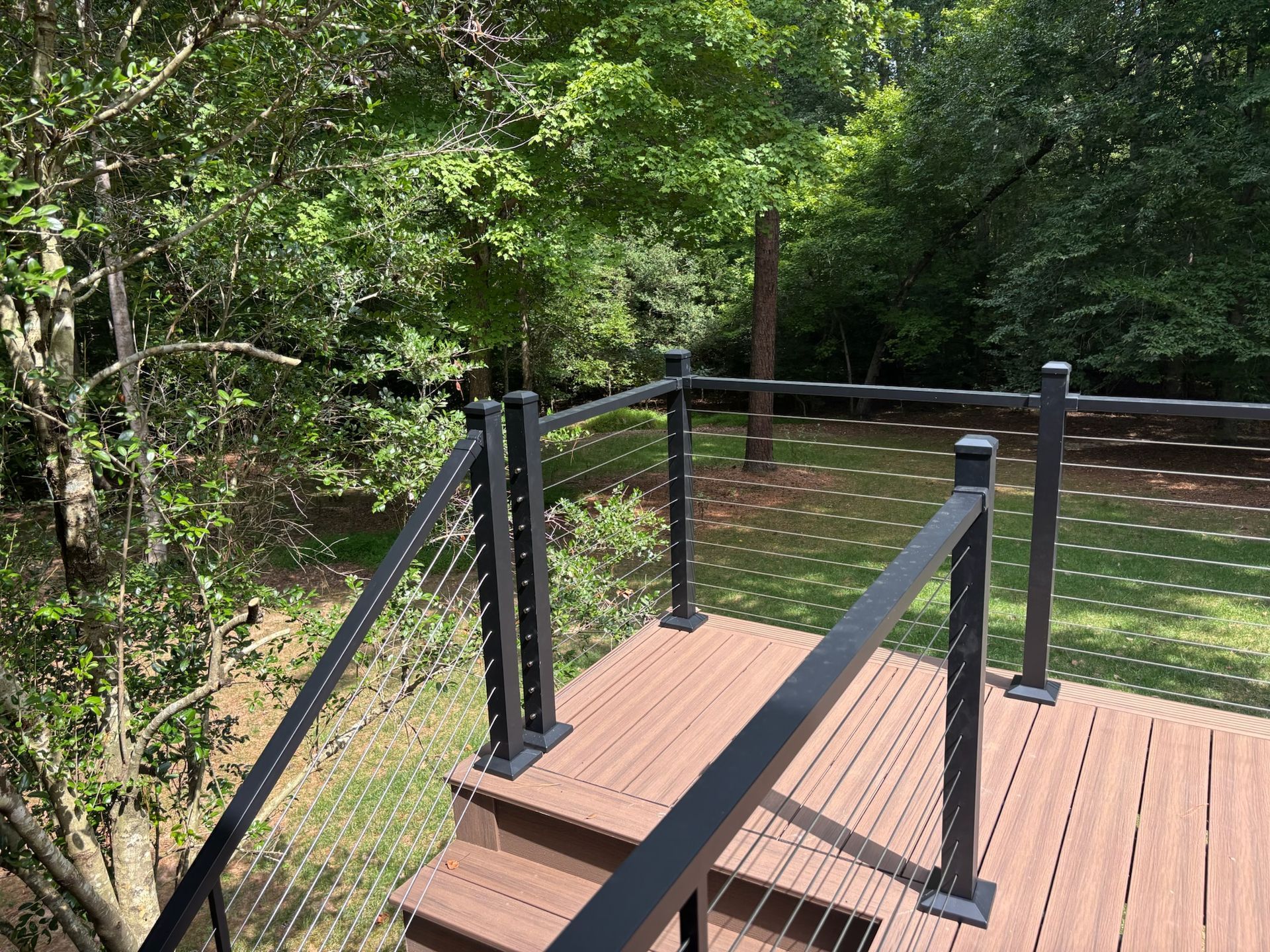 Wooden boardwalk platform with black railings in a wooded area