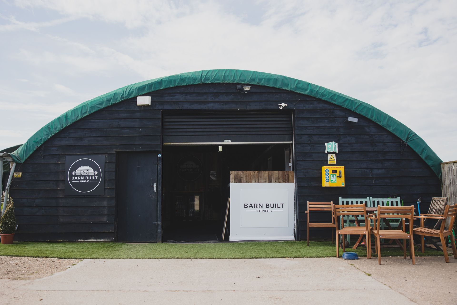 Black wooden arched building with open entrance, outdoor seating.