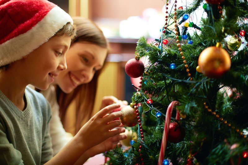 A person in a Santa hat and another person decorating a Christmas tree with ornaments.