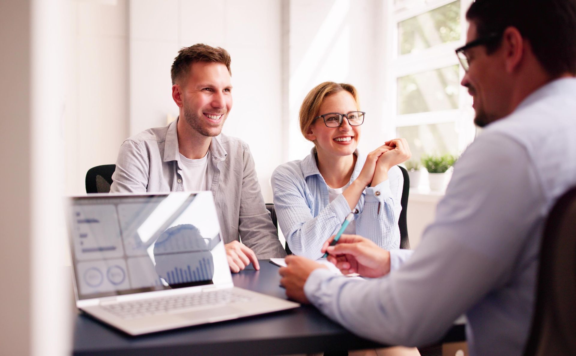 Couple smiling while meeting with a professional at a desk with laptop.