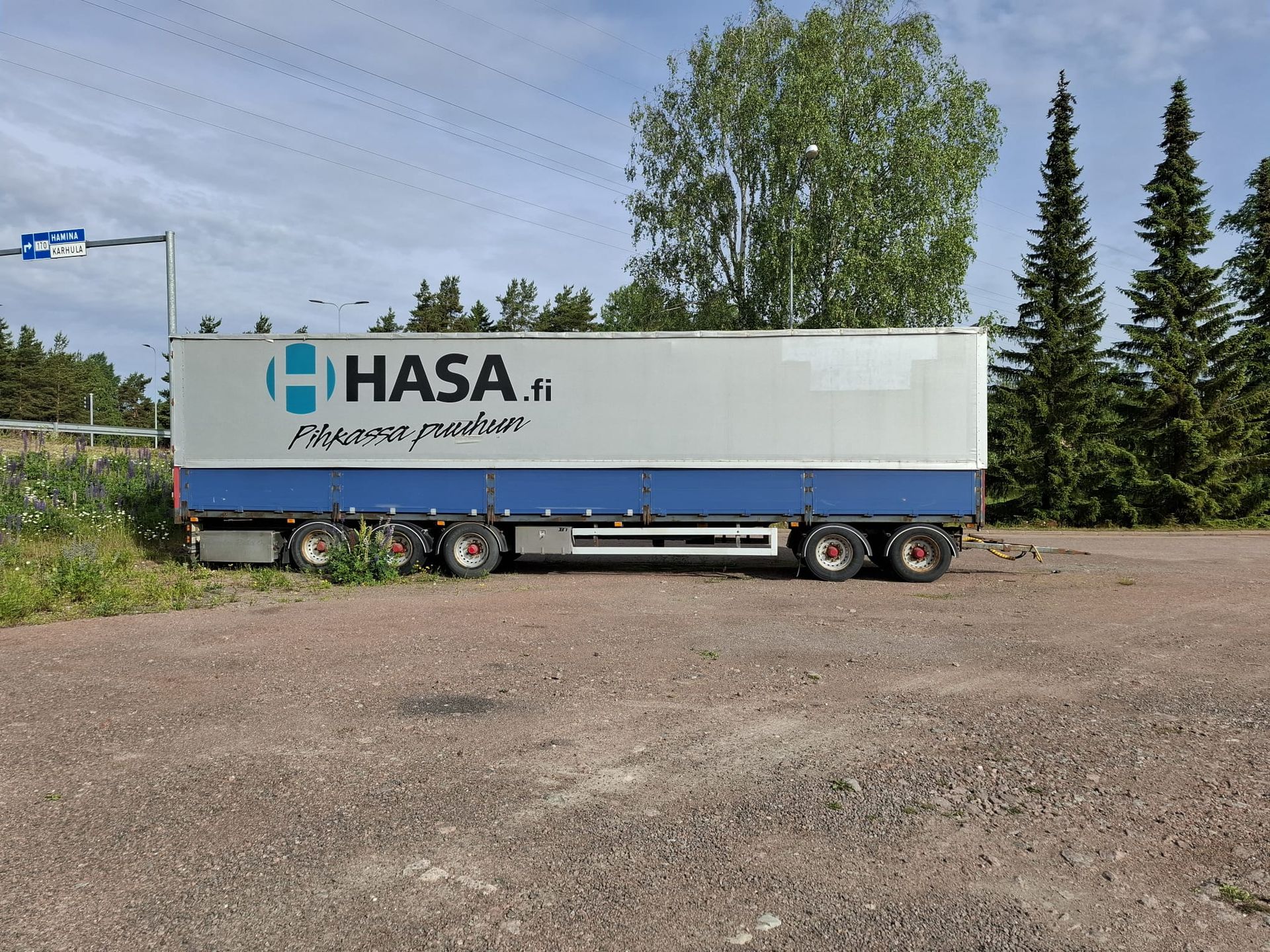 Valkoinen ja sininen hasa perävaunu on pysäköity soratontille.
