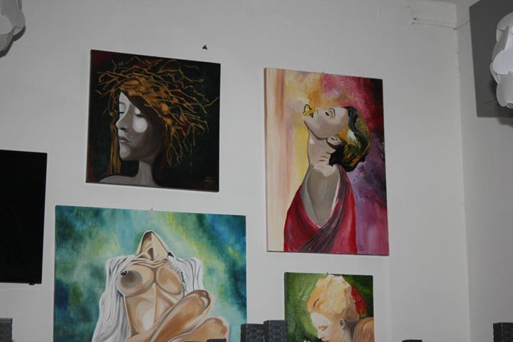 Ritratti colorati esposti su una parete bianca in un ambiente simile a una galleria.