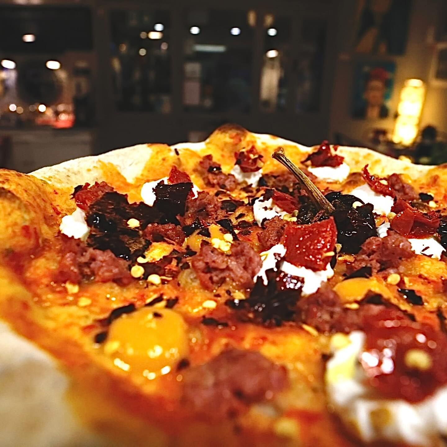 Primo piano di una pizza ricca di formaggio e condimenti, illuminata dalla calda luce del ristorante.