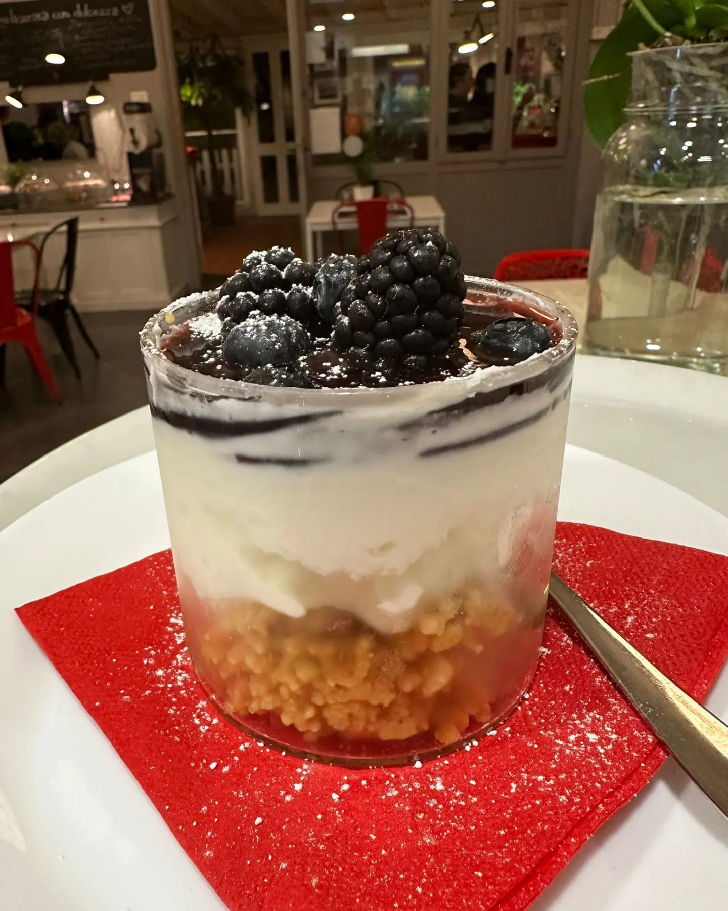 Parfait di dessert con more in un bicchiere su un tovagliolo rosso a un tavolo di ristorante.
