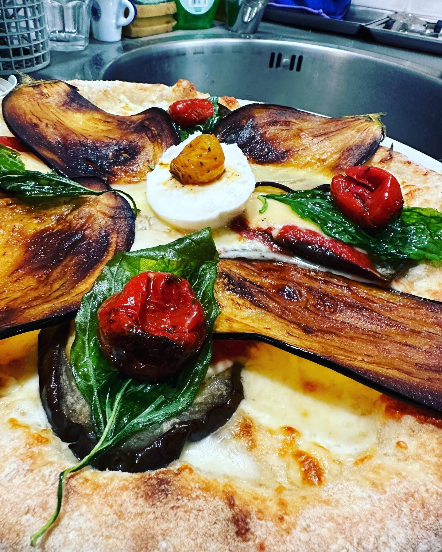 Pizza condita con melanzane arrostite, basilico, pomodorini e burrata, su una teglia da forno.