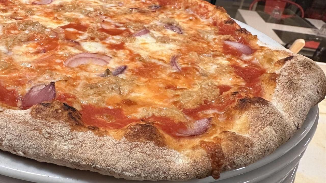 Primo piano di una pizza al salame piccante in una teglia di metallo, con formaggio dorato e una crosta spessa.
