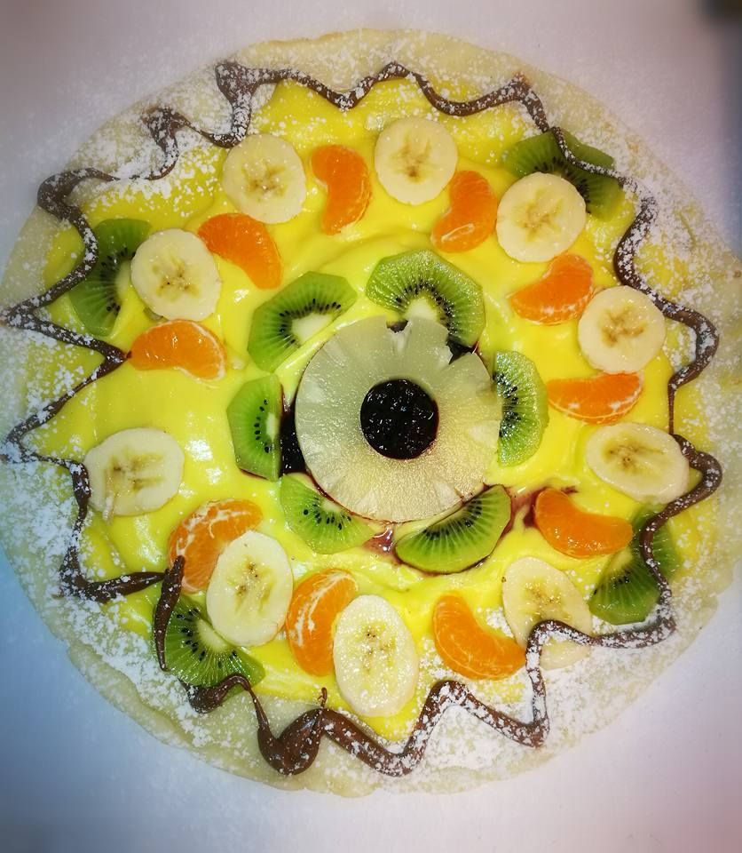 Torta rotonda con frutta, kiwi, banana, fette d'arancia e ripieno nero, servita su un piatto bianco.