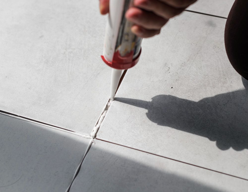 A person is applying a sealant to a tile floor.