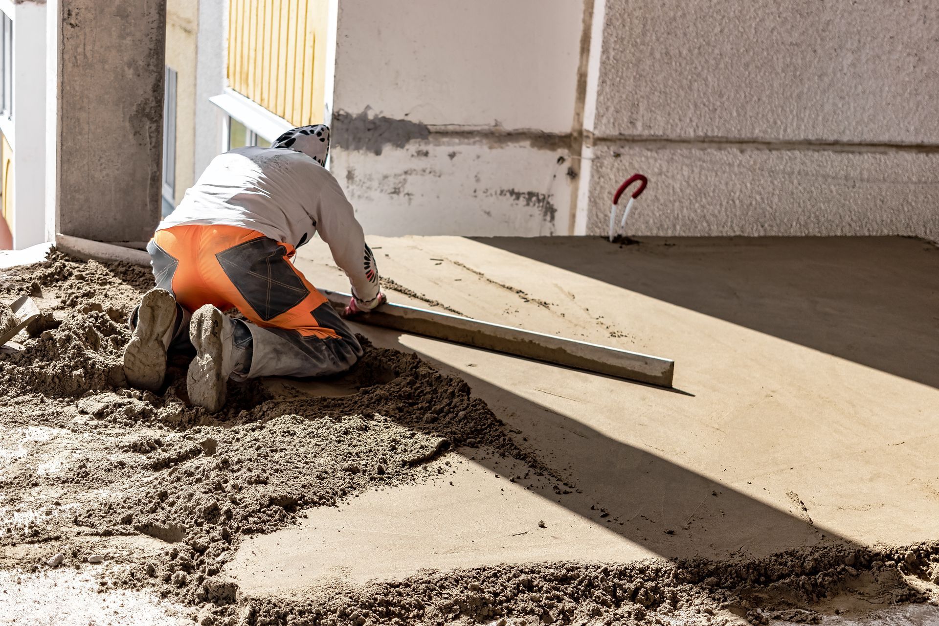 A man is laying concrete on the ground with a level.