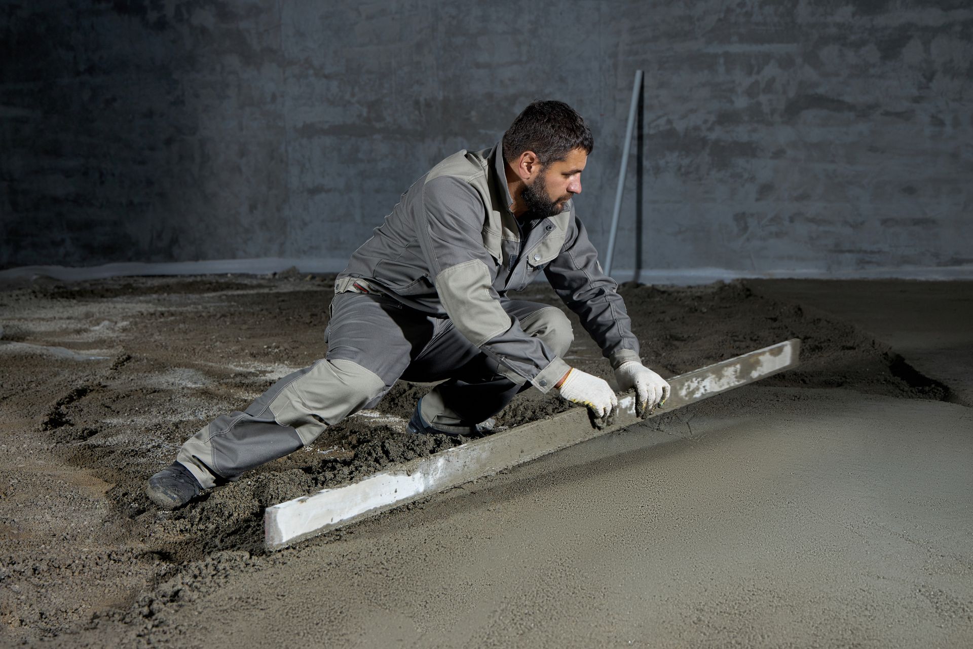 A man is laying concrete on the floor with a level.
