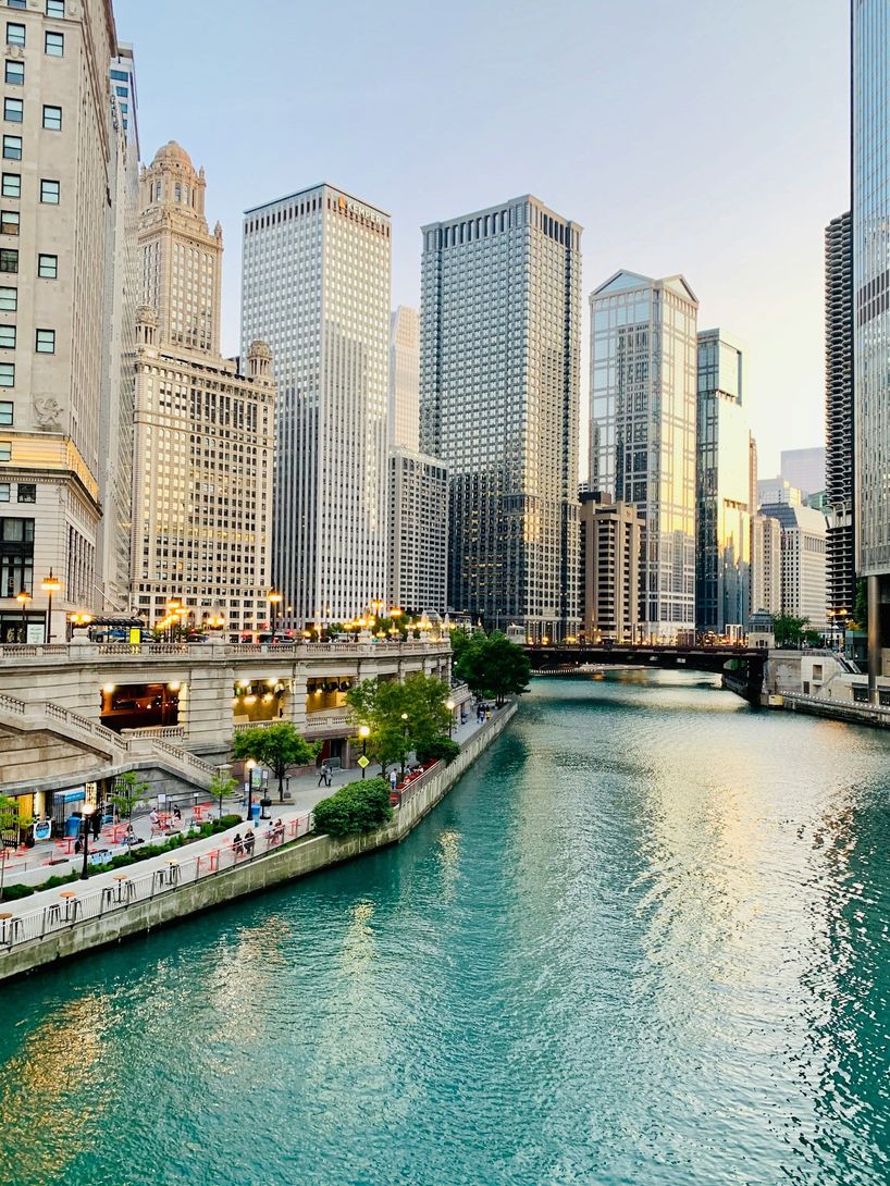 Chicago River lined with tall skyscrapers, a turquoise waterway, and a sunlit riverside walkway
