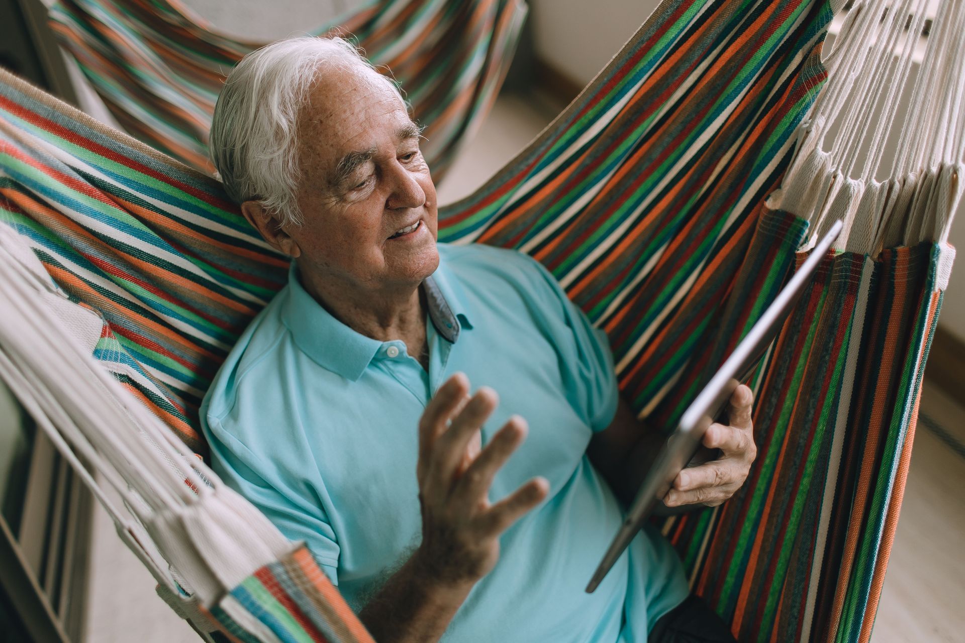 Man relaxing in a striped hammock, smiling while holding a book or tablet.