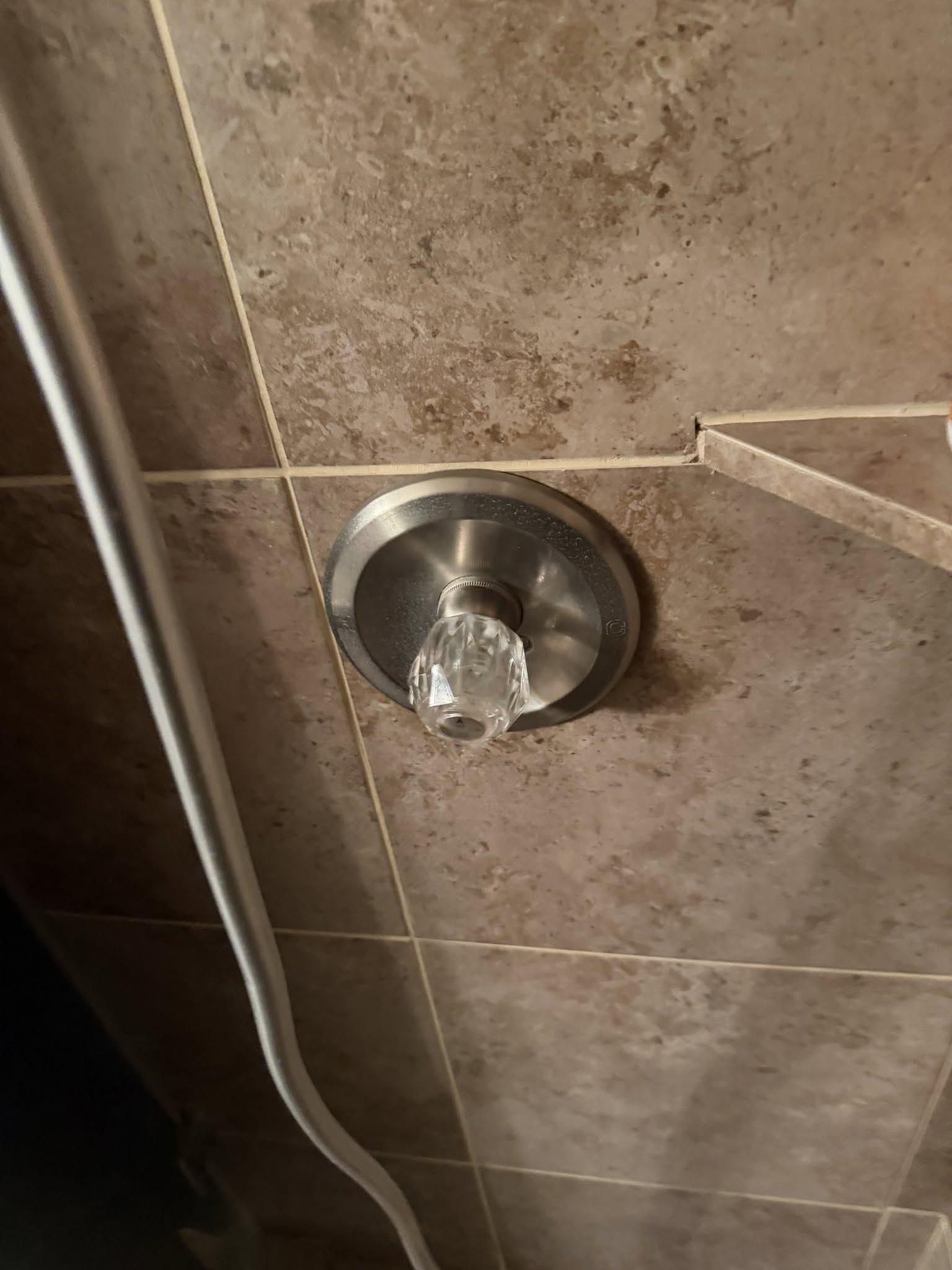 Close-up of a stainless steel shower control knob on beige tiled bathroom wall