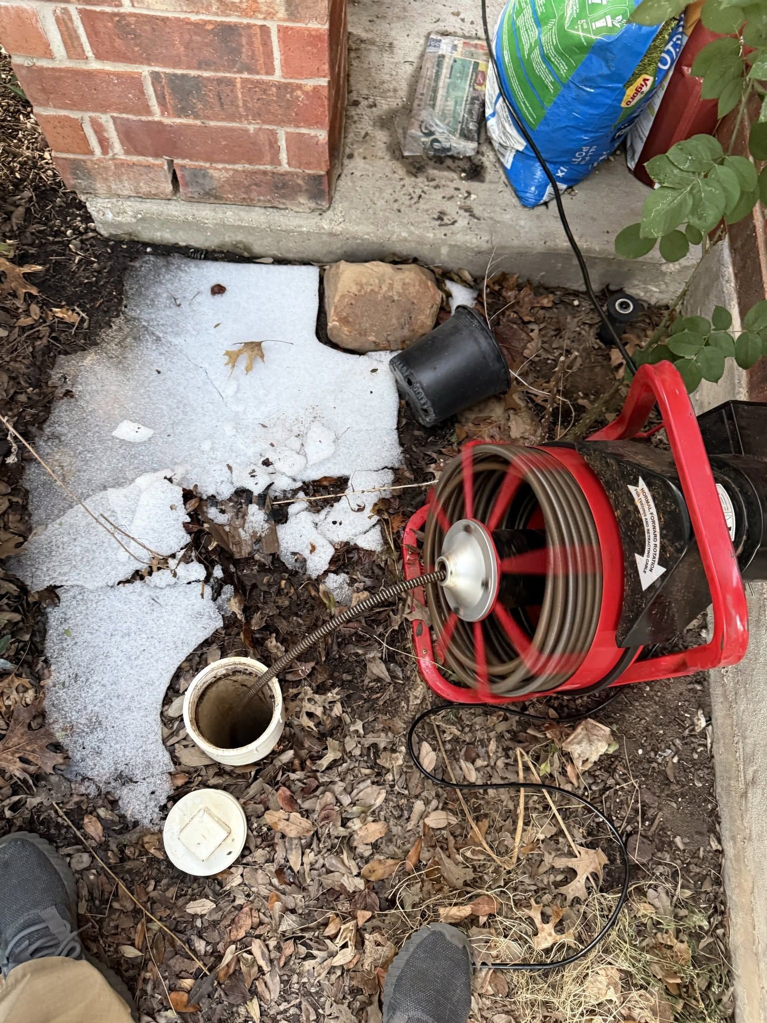 Outdoor corner with a red heater fan, white PVC pipe, and debris beside a brick wall