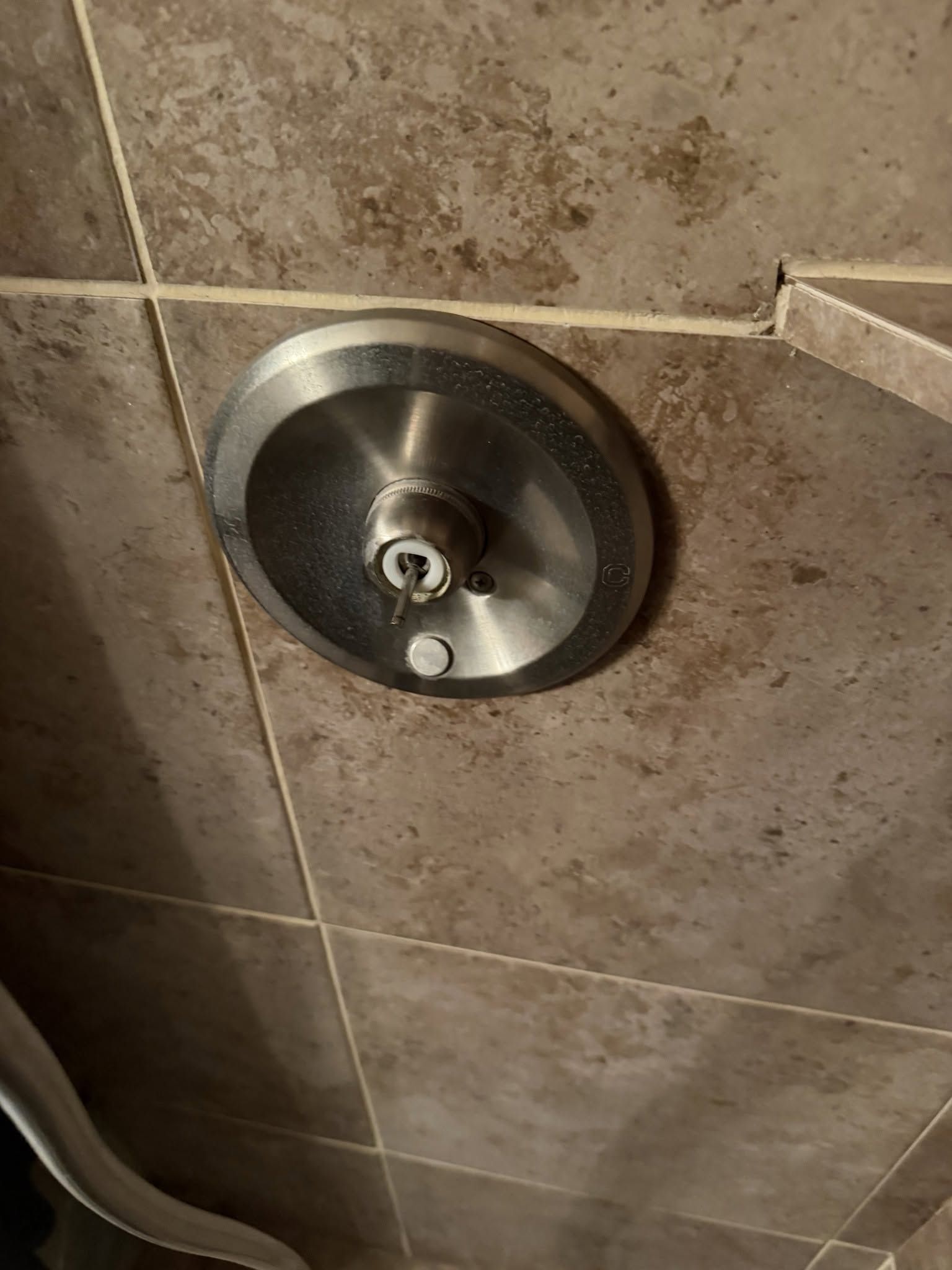 Round chrome shower control on beige tiled wall with a small protruding knob.
