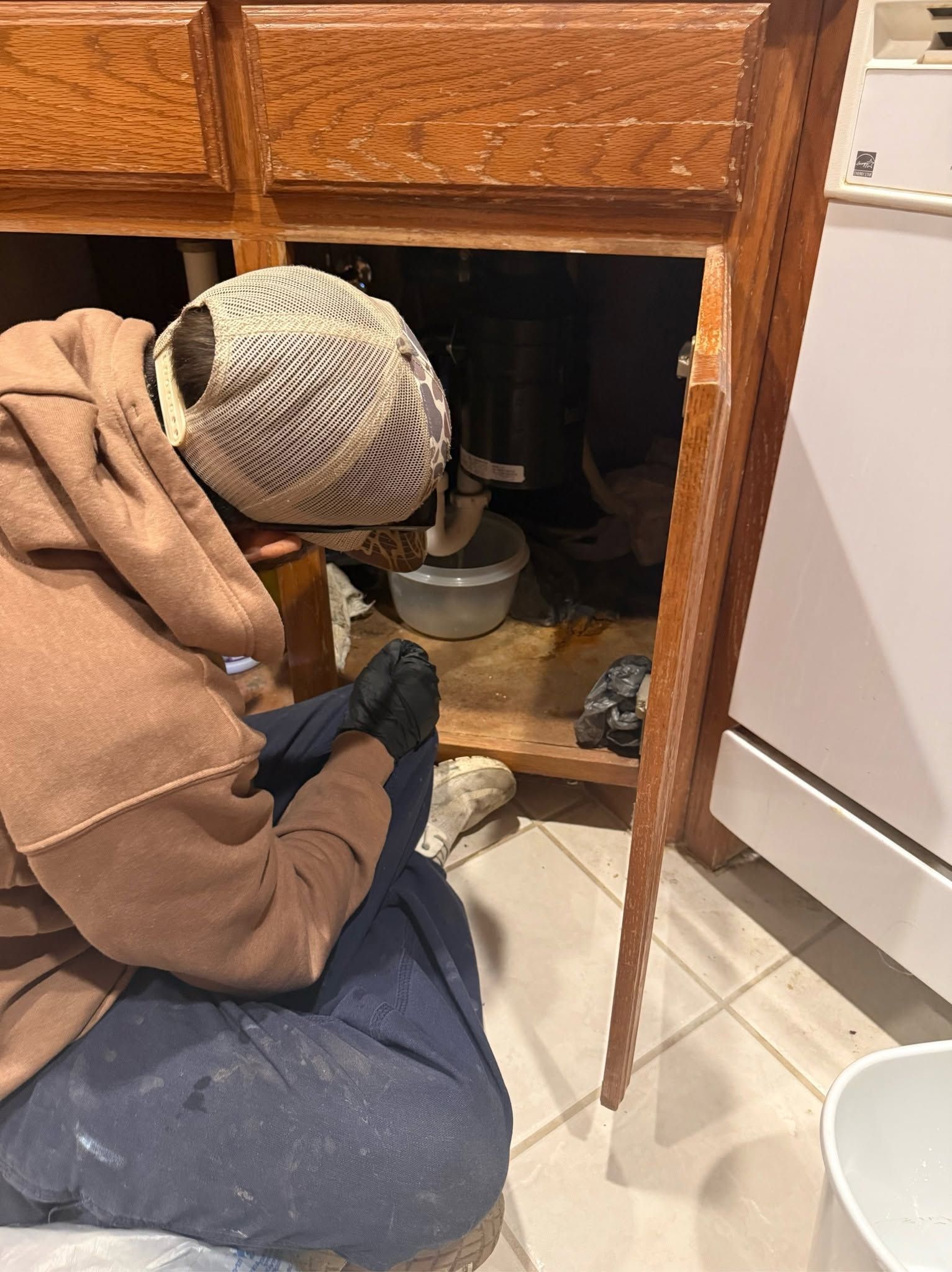 Person kneeling under a cabinet, cleaning a dark nook with a cloth in a kitchen.