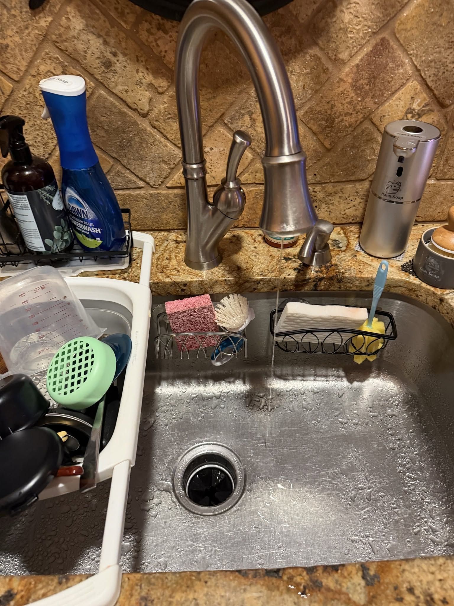Kitchen sink with running faucet, dish soap, sponge, and dishes in a cluttered counter area