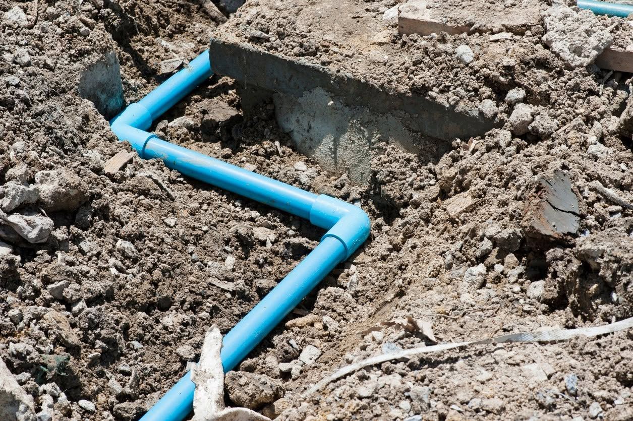 Blue plastic pipe runs through a dirt trench beside a concrete opening.