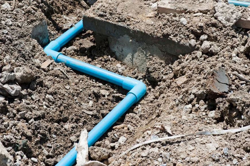 Blue plastic pipe runs through a dirt trench beside a concrete opening.
