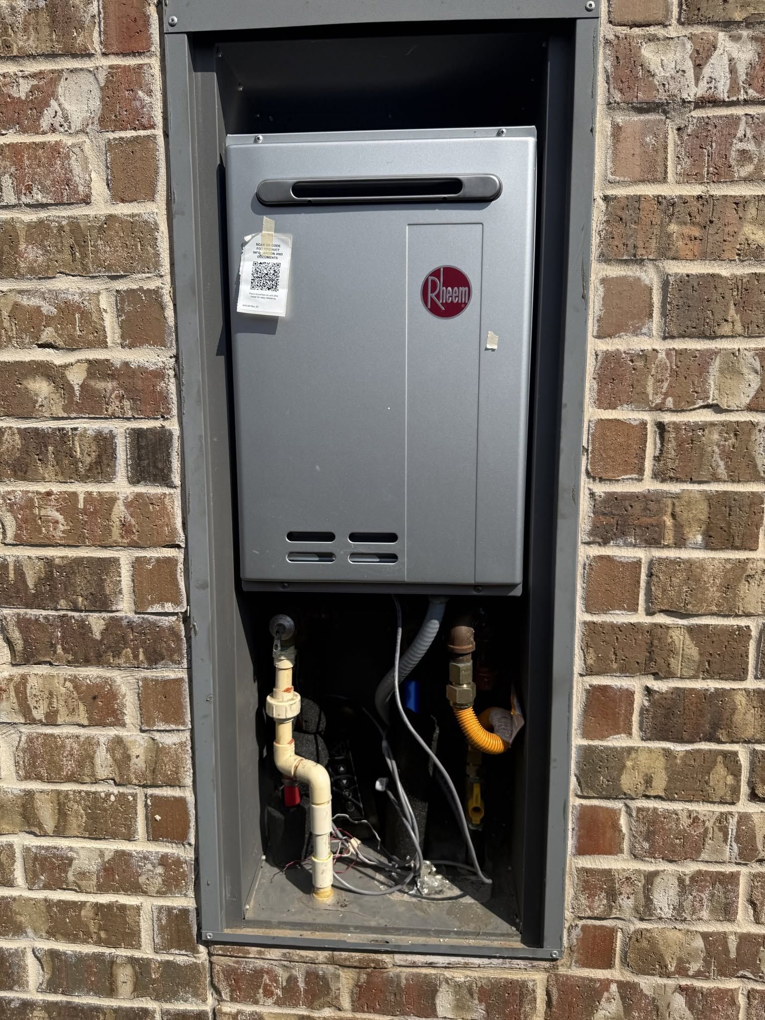 Gas meter mounted in a brick wall recess with exposed pipes and a hanging lockout tag