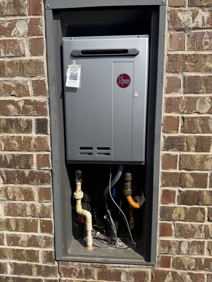 Gas meter mounted in a brick wall recess with exposed pipes and a hanging lockout tag