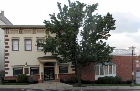 Street view of a beige and red brick building with a large tree in front