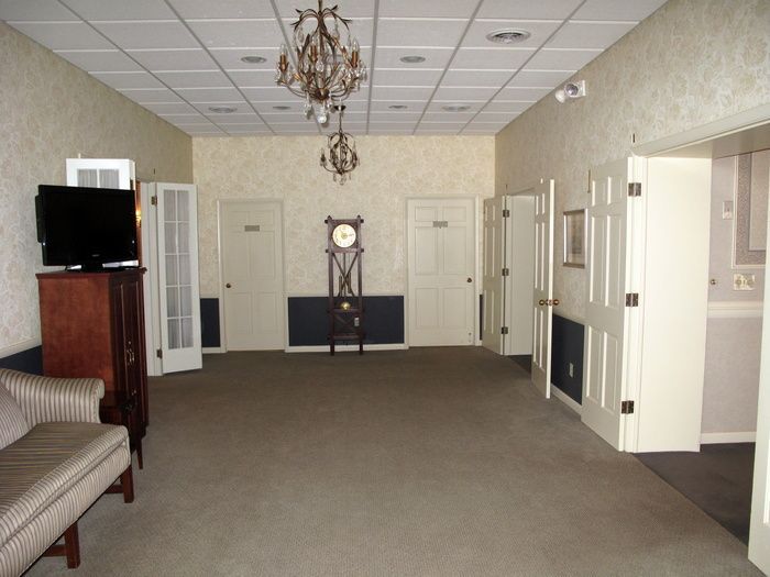 Empty beige lobby with carpet, white doors, chandelier, TV, and a large clock on the back wall