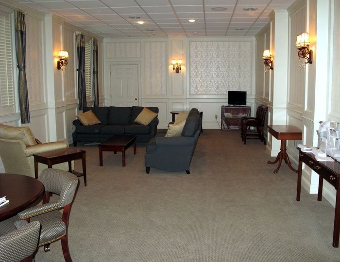 Quiet lounge with beige carpet, dark sofas and chairs, wall sconces, and a small TV on a side table.