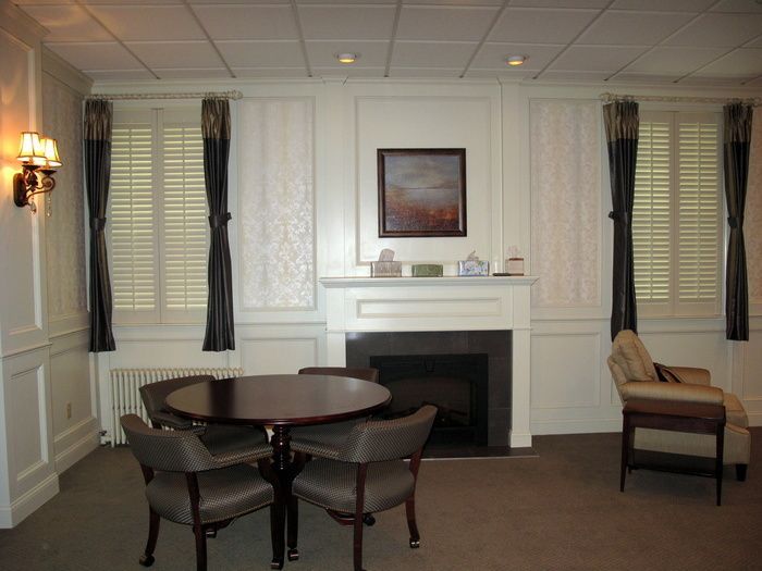 Empty lounge with round table, chairs, fireplace, framed art, and wall sconces on white paneled walls