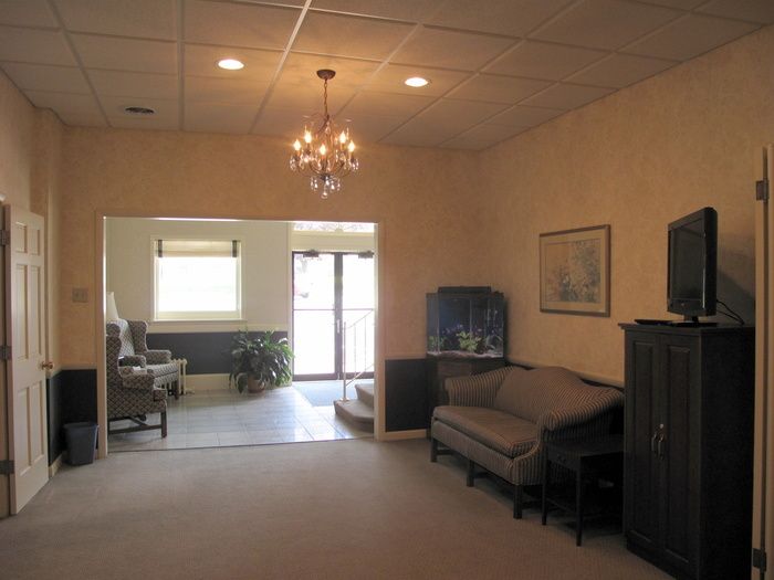 Empty beige living room with chandelier, sofa, TV, and large opening to a bright adjoining room