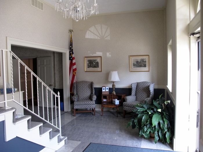Small foyer with stairs, two patterned chairs, table lamp, wall art, and a large green plant.