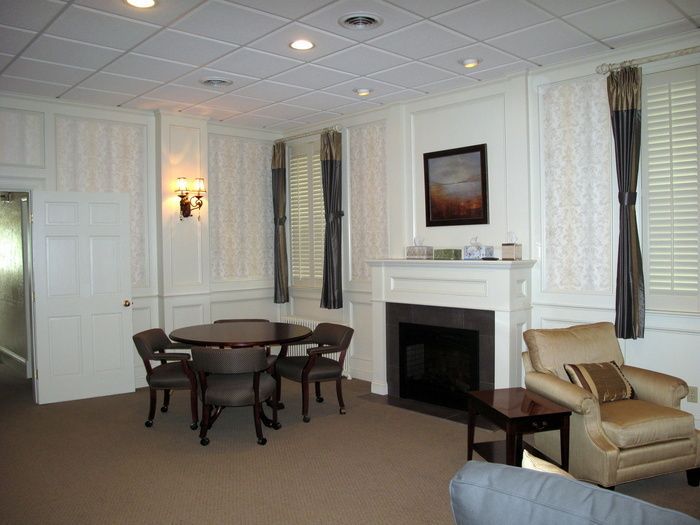 Bright living room with dining table, fireplace, white paneled walls, and beige armchair