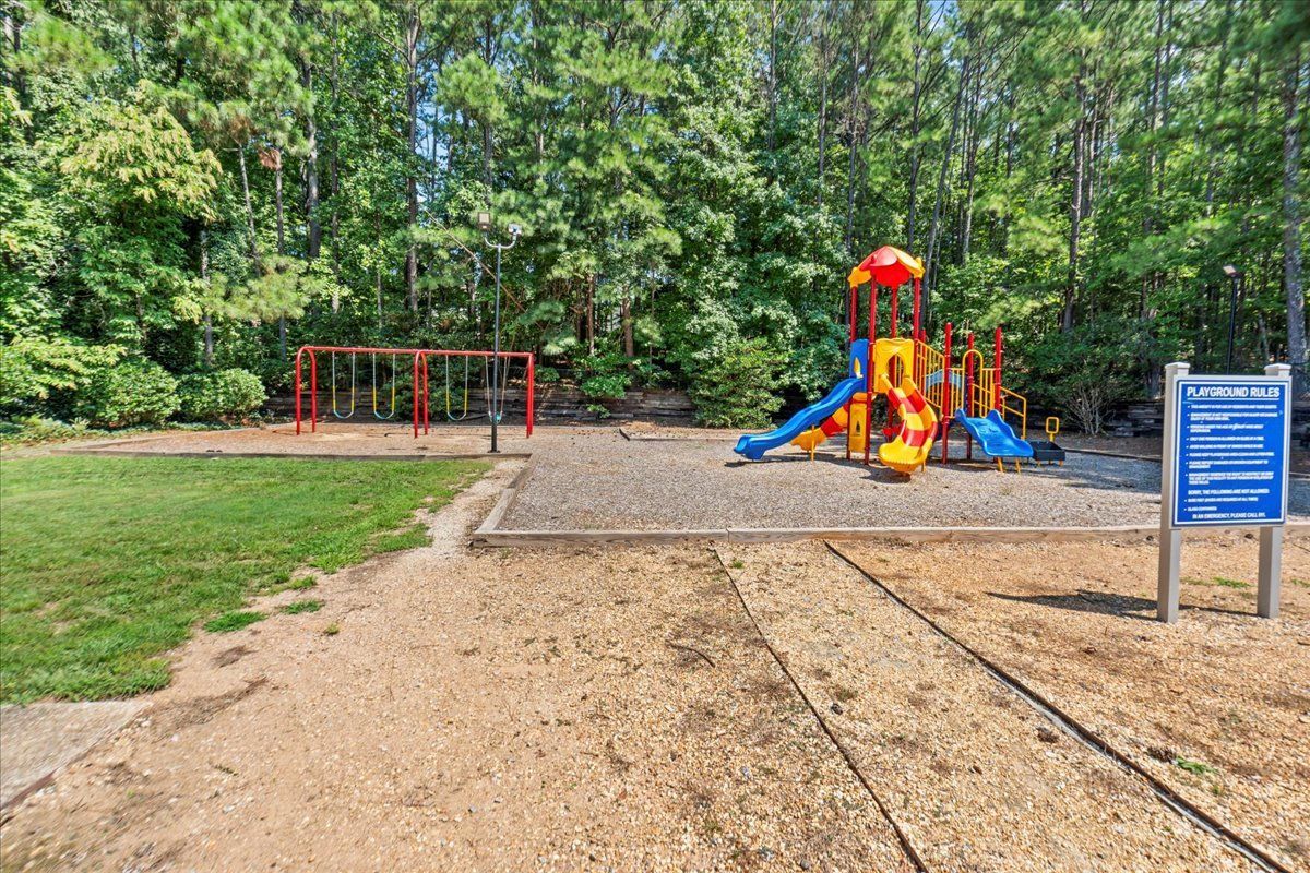A playground with a red swing set and a colorful multi-level slide structure set in a wooded, grassy park area.