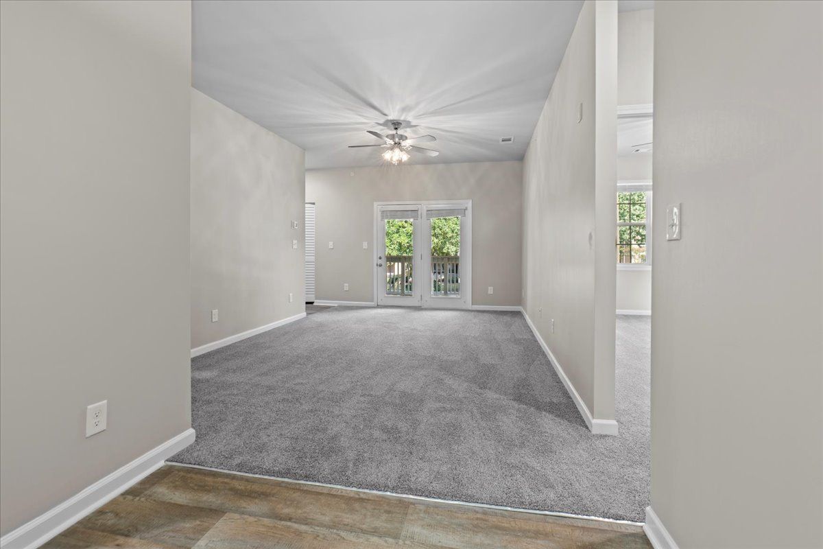 An interior view from a hallway looking into a carpeted living room with a ceiling fan and sliding glass doors.