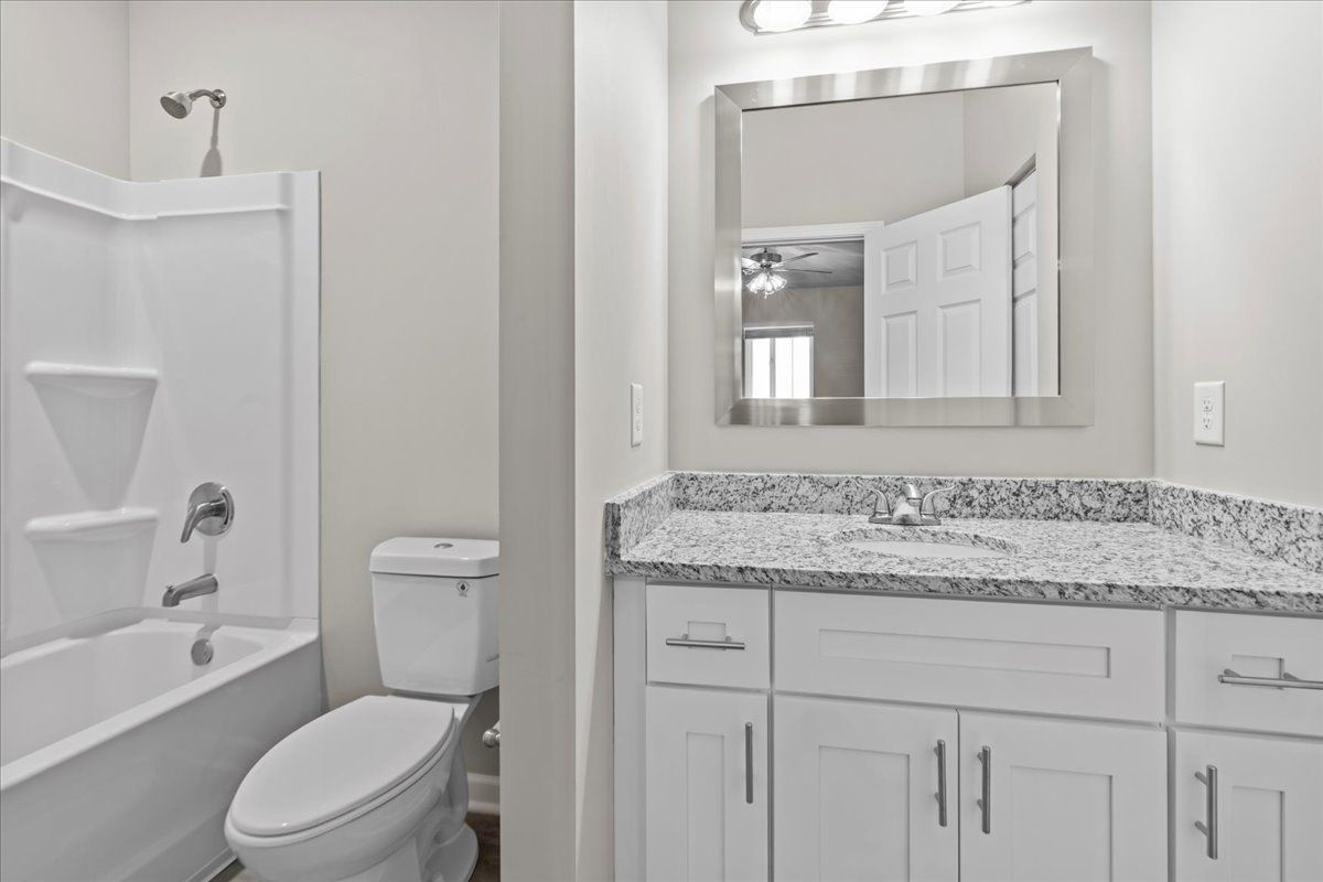 A bathroom with a white tub-shower combo, toilet, and vanity with a granite countertop and large mirror.