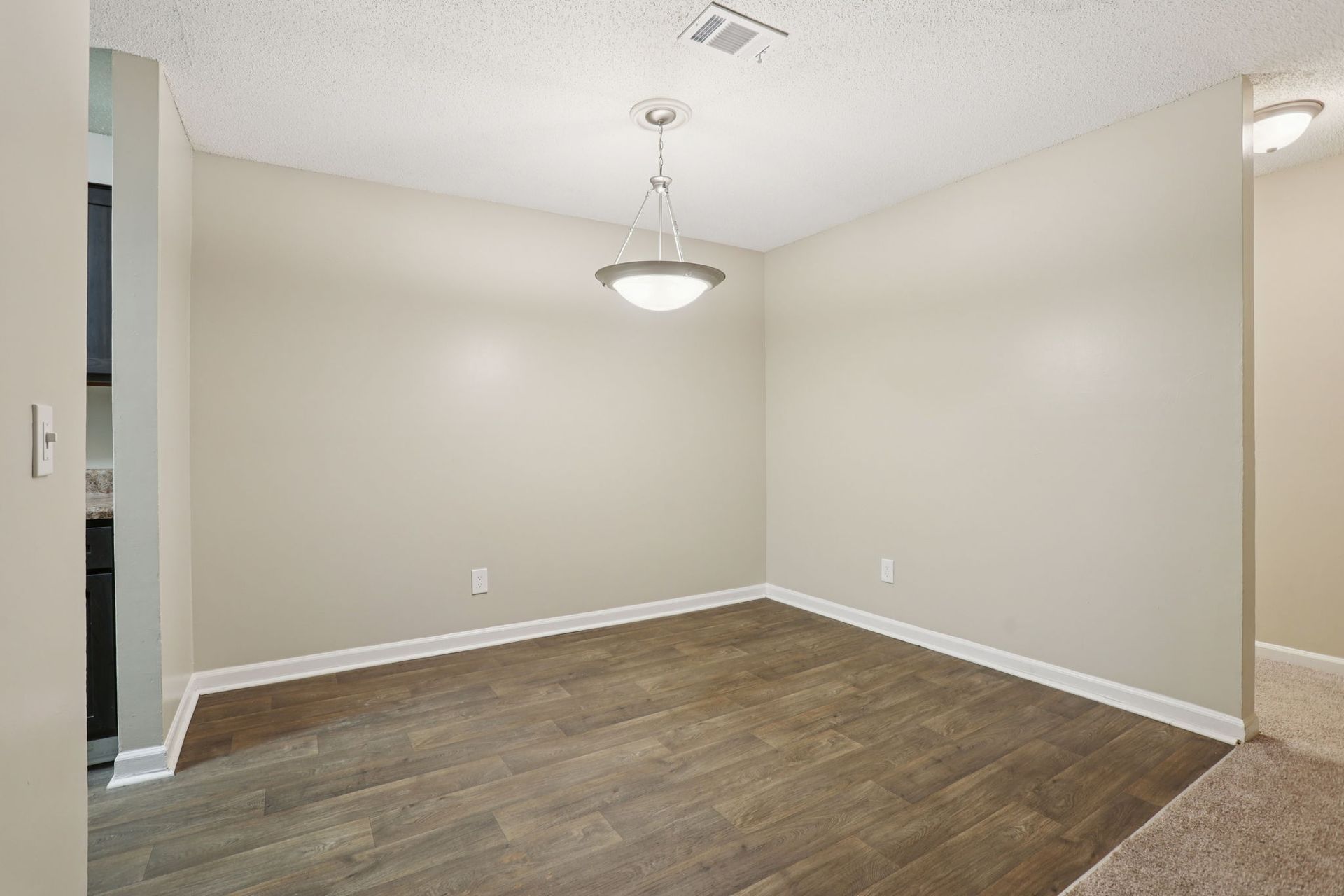 Empty dining room with beige walls, wood-look flooring, and a modern pendant light fixture.